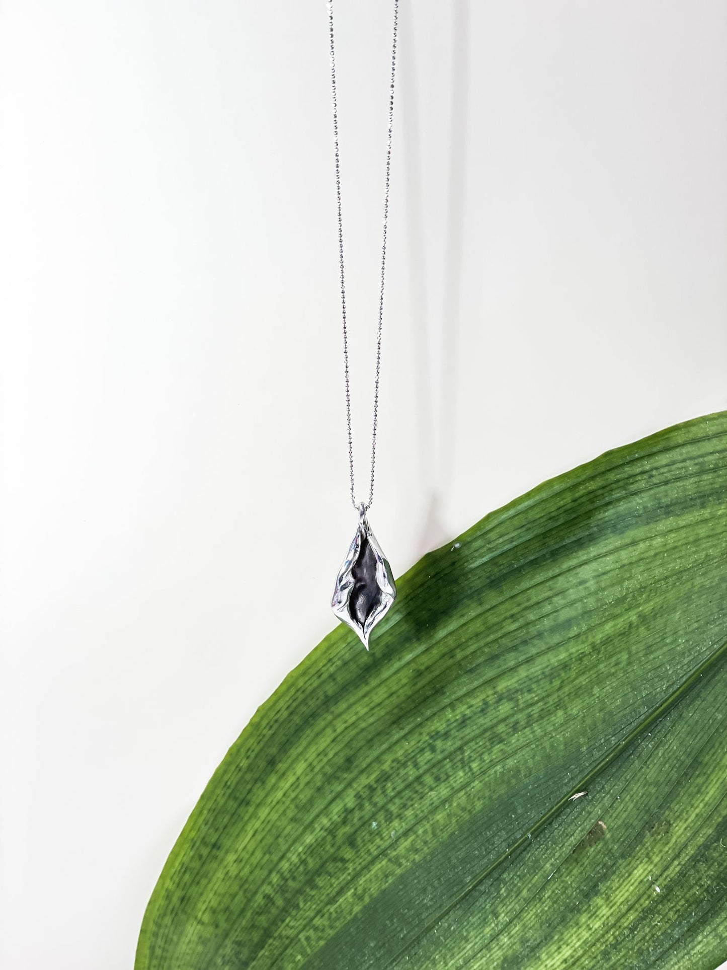 Graceful Foliage Silver Charm Necklace with leaf design hanging elegantly above a green leaf backdrop, part of silver jewelry collection.