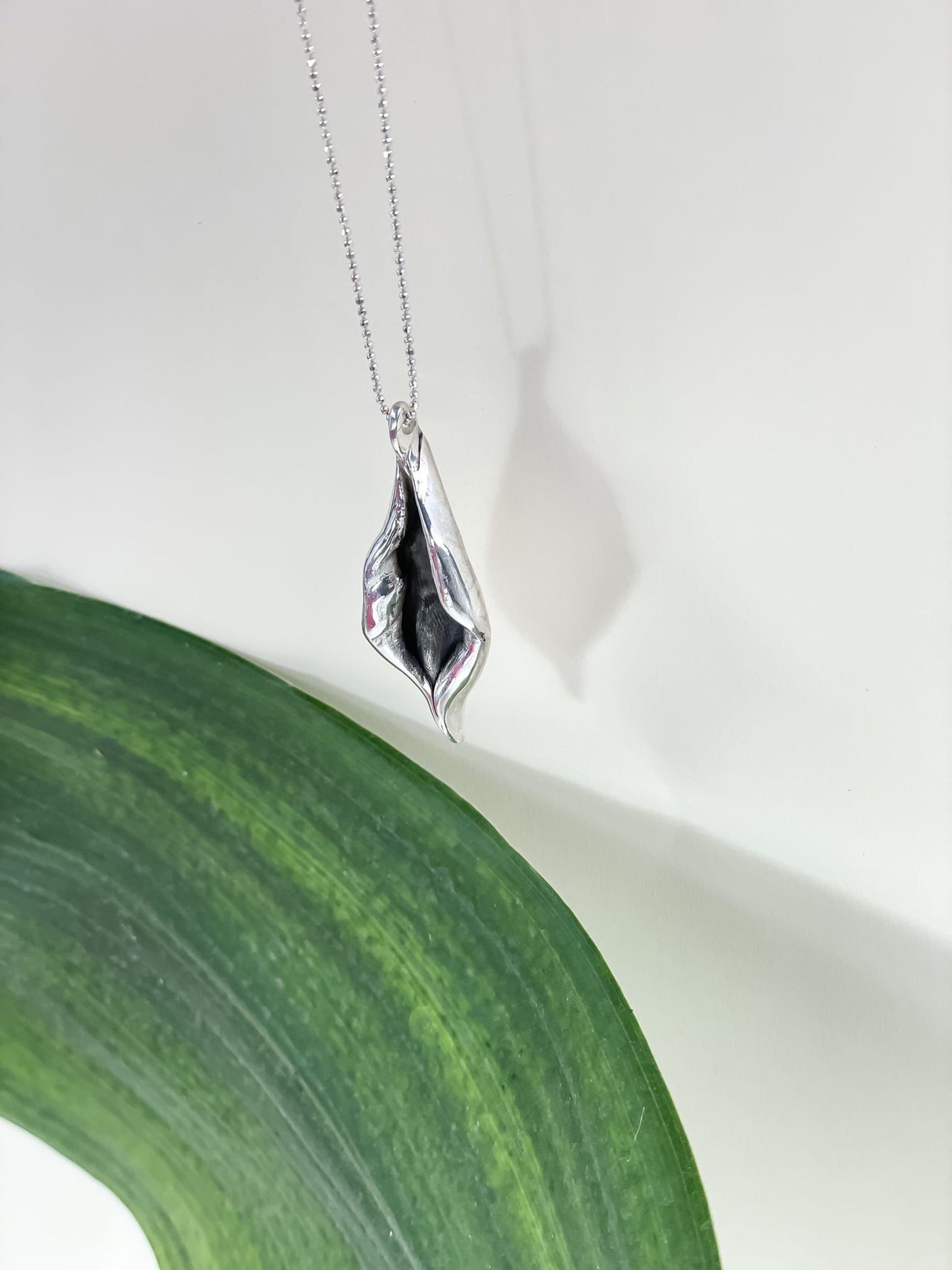 Graceful Foliage Silver Charm Necklace inspired by nature's elegance with meticulously crafted leaf-shaped design against a green leaf background.