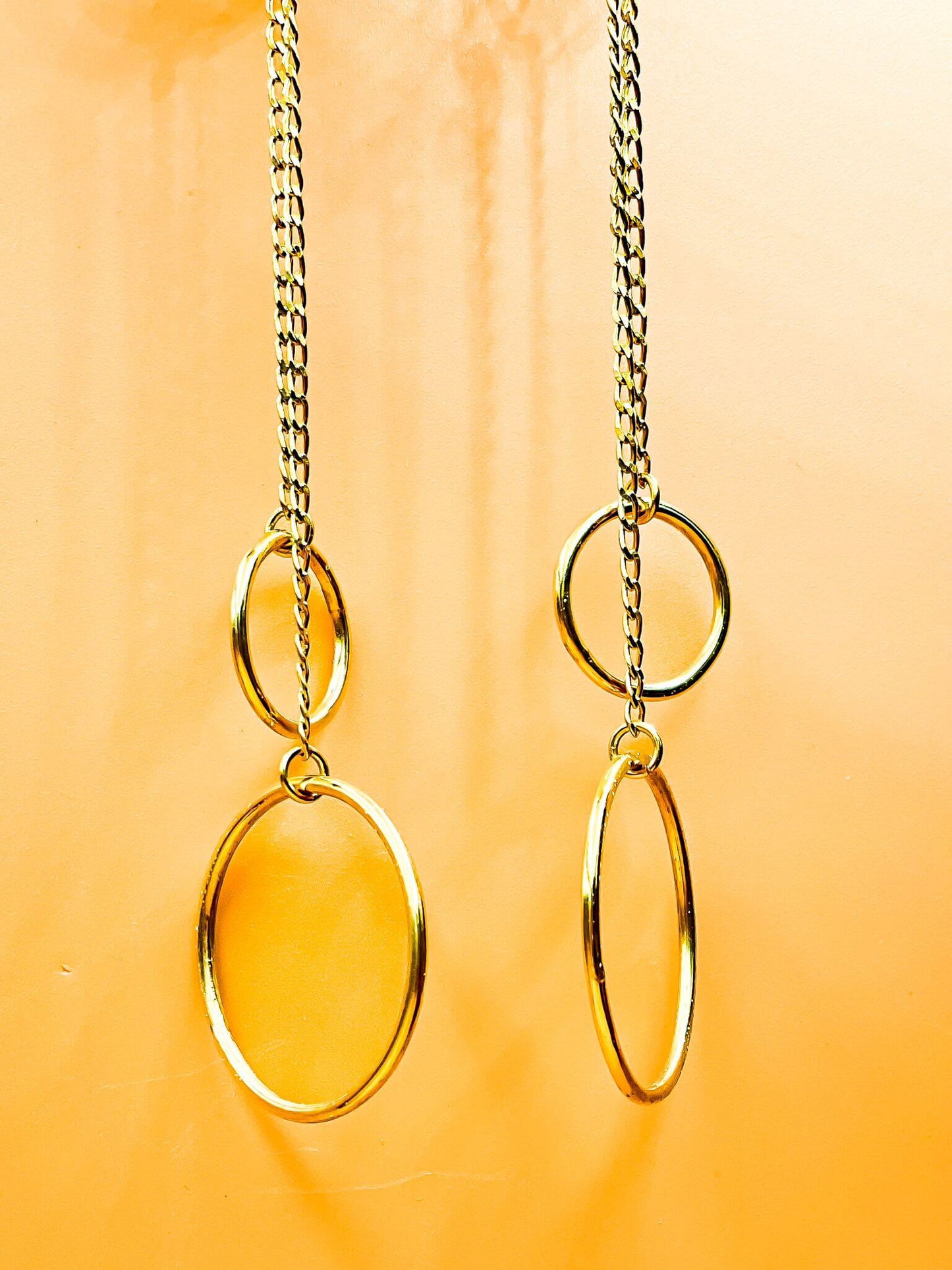 Harmony Swing Earrings with 18-carat gold plating and sterling silver base showcasing playful hoops suspended from long chains against a peach background.