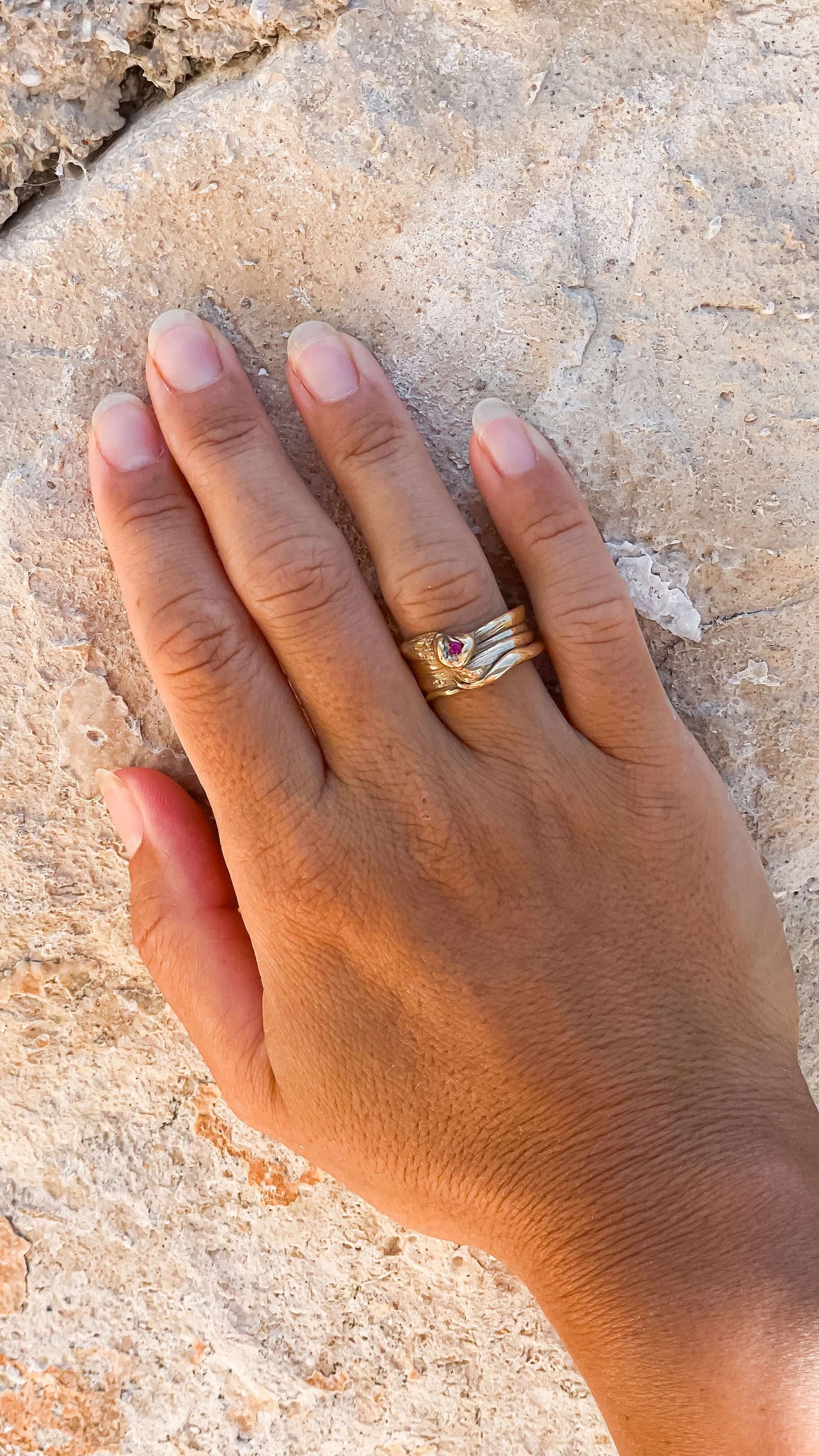 Hand wearing a unique handcrafted bronze Mitsuro Hikimi ring with a sparkling zircon stone, showcased against a textured stone background.