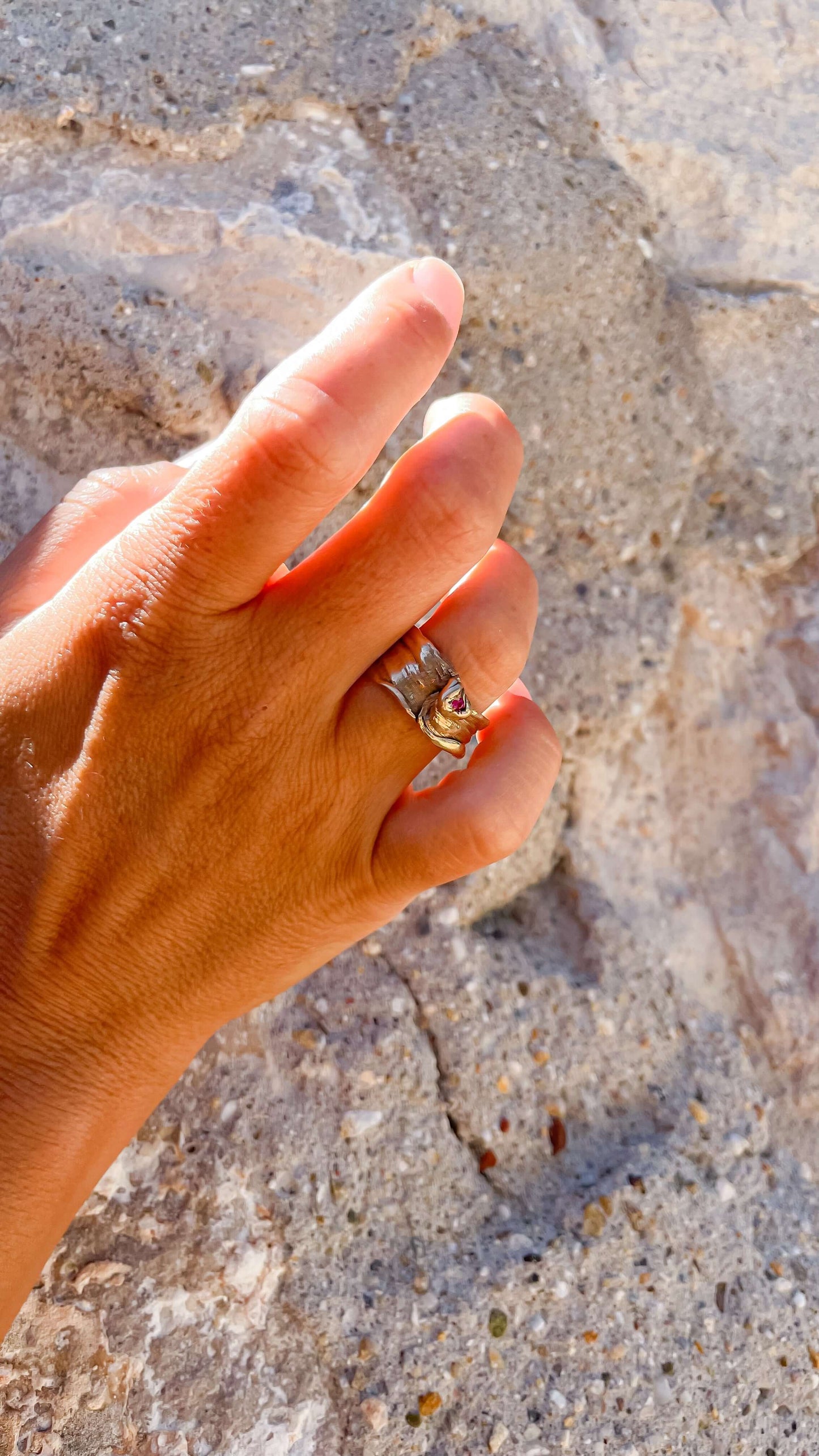 Hand wearing a handcrafted bronze Mitsuro Hikimi ring with a sparkling Zircon stone against a textured stone background