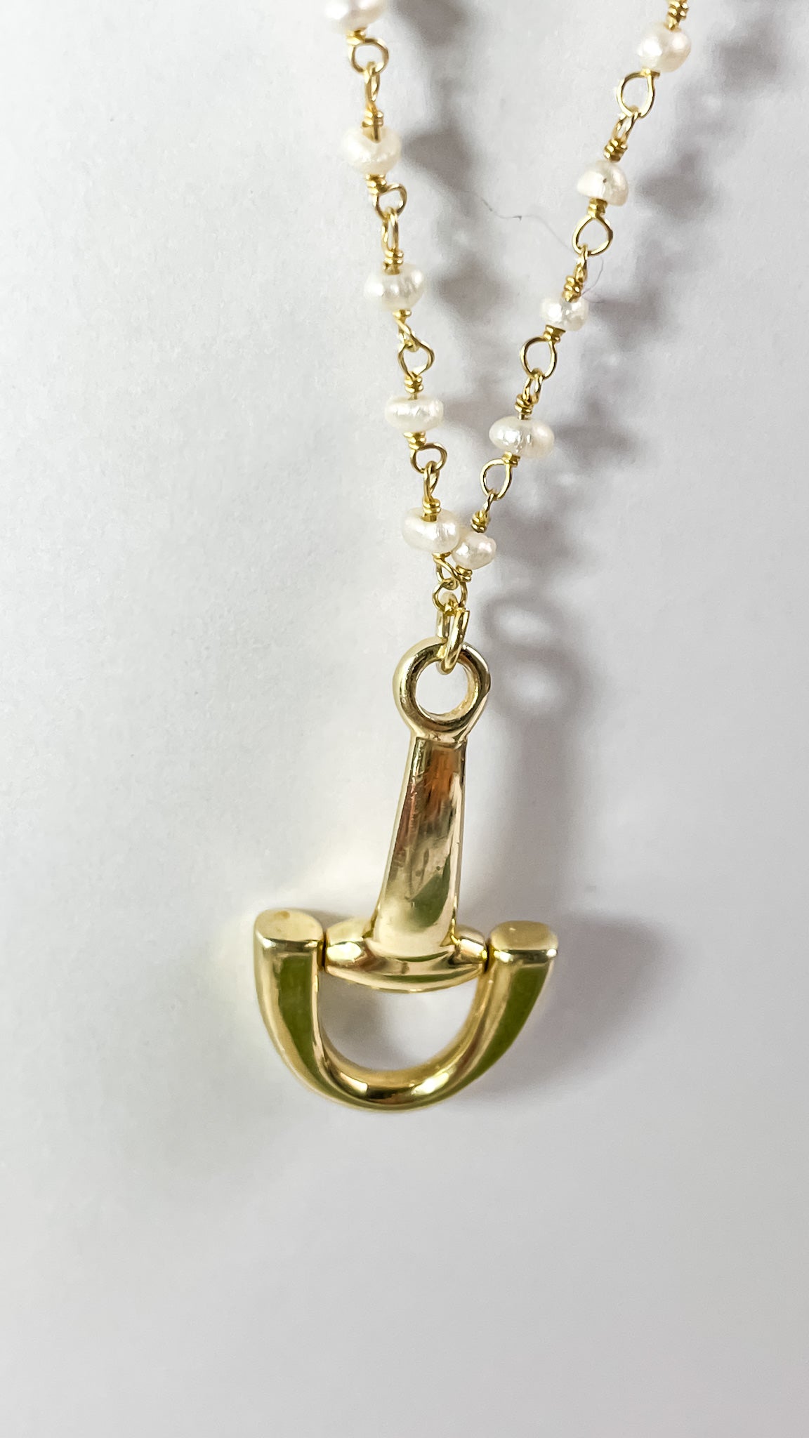 Gold horse bit pendant necklace with pearl chain on white background