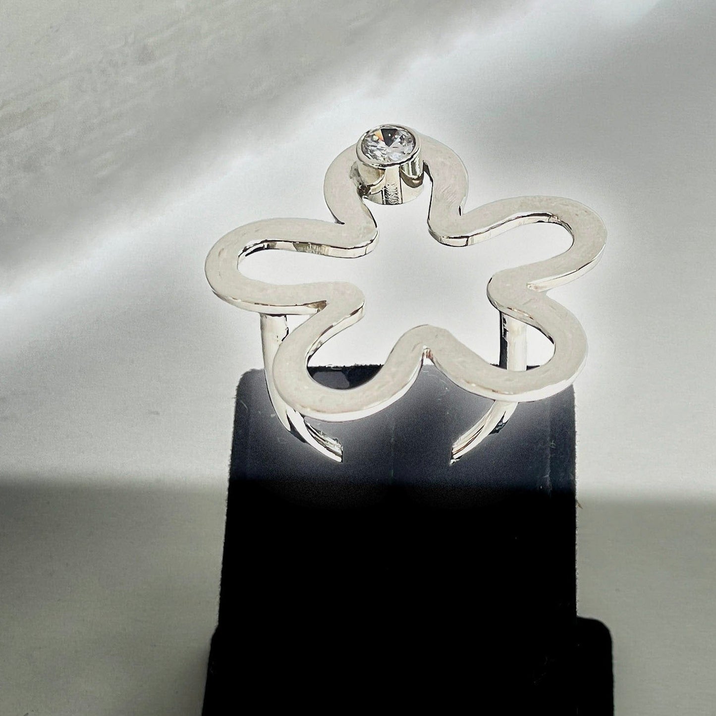 Sterling silver floral ring with a delicate flower design and a central gemstone on display stand.