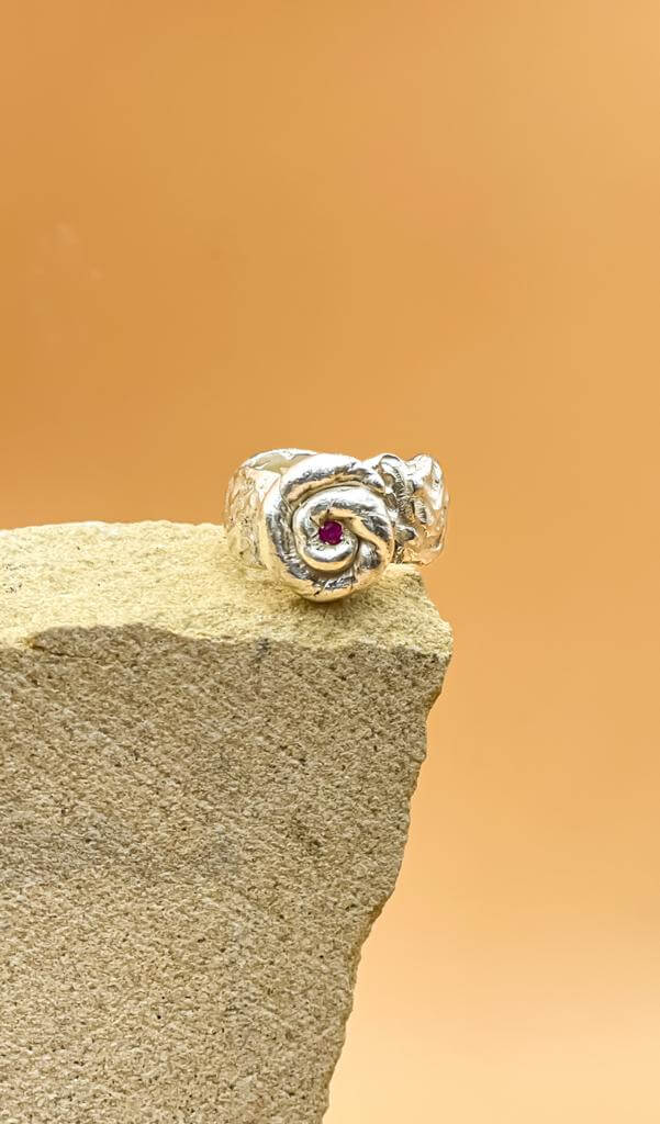 Rose Radiance Ring in 925 sterling silver with a zircon stone, displayed on a textured rock against a warm background.